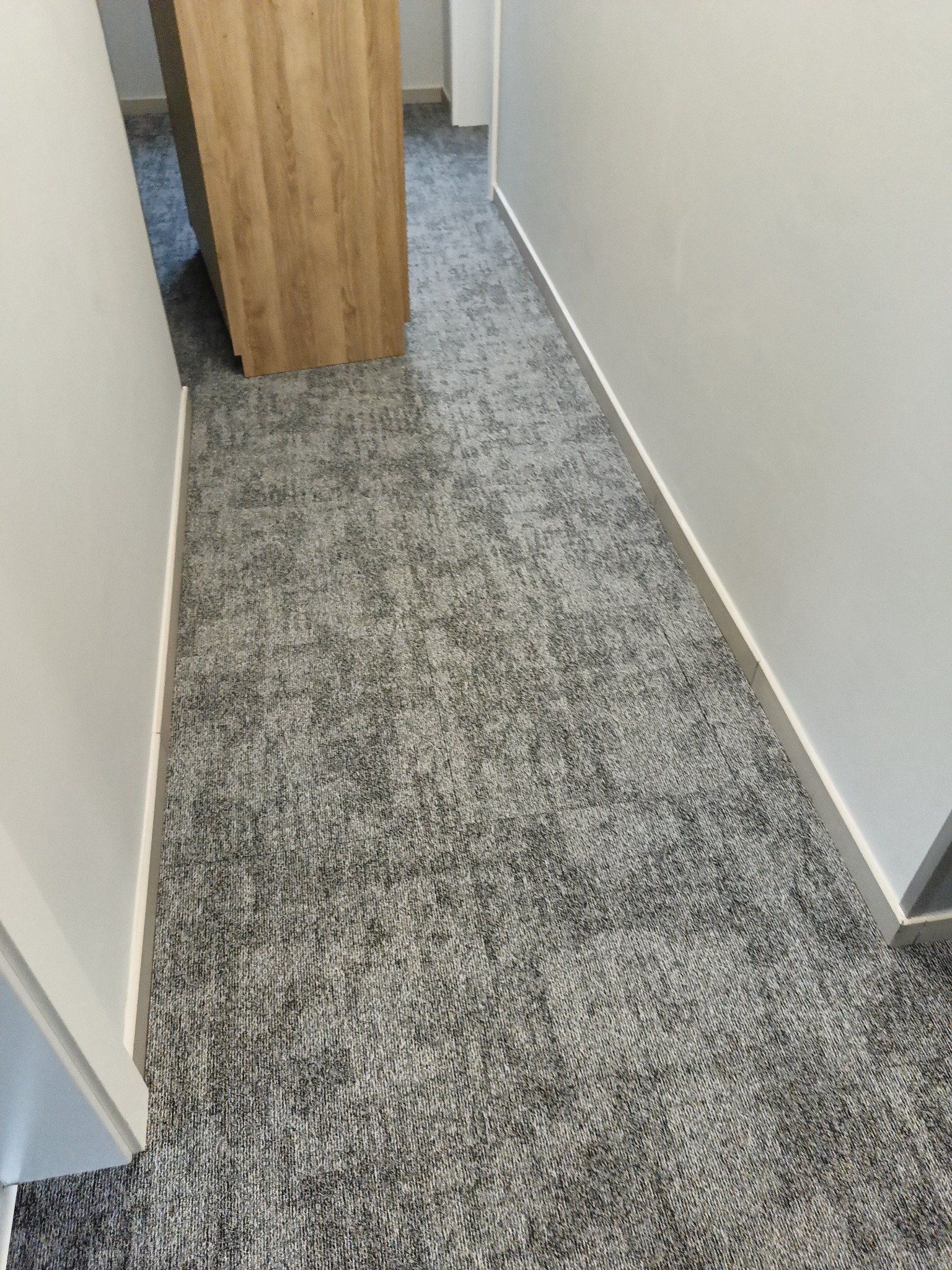 Szara wykładzina dywanowa w korytarzu biurowym w Gdyni, widok z góry, z listwami przypodłogowymi.