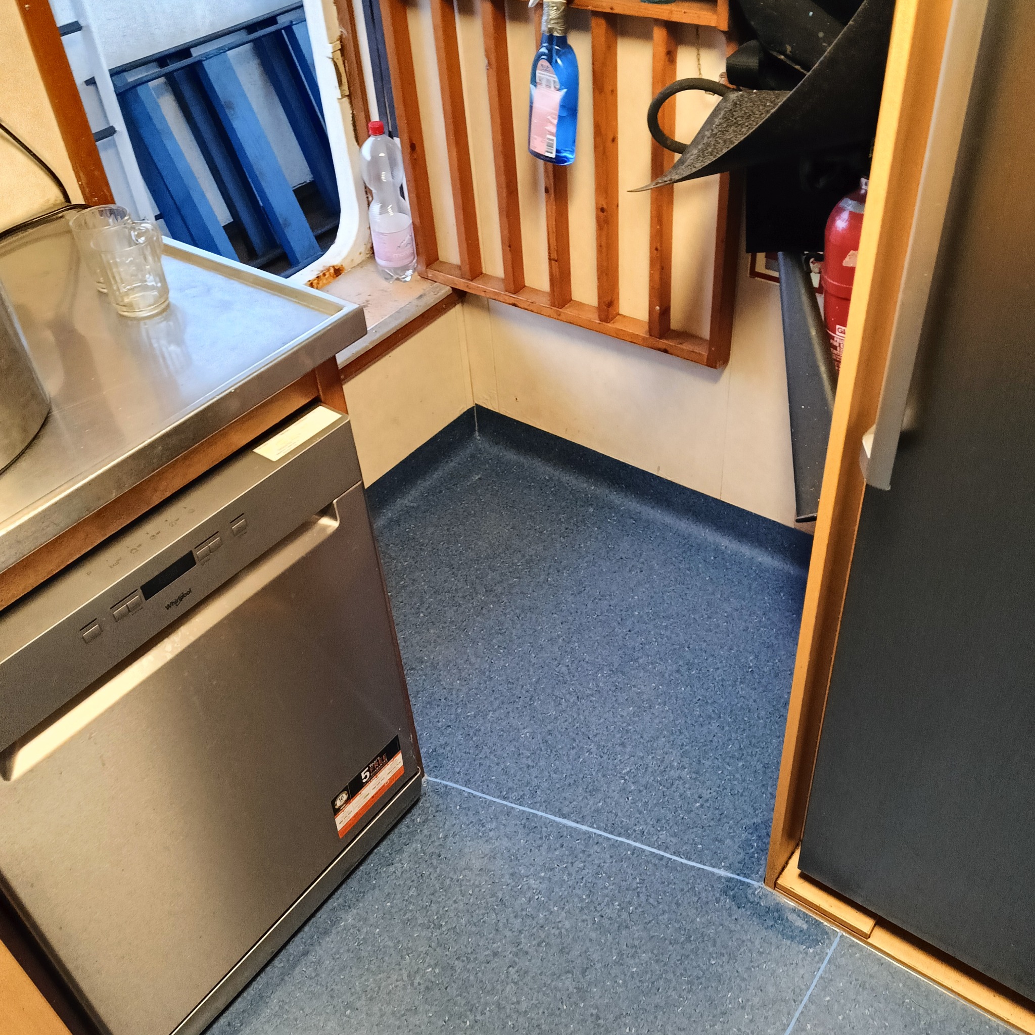 Niebieska, drobnoziarnista posadzka z PCV w pomieszczeniu gospodarczym, widoczna zlewka, butelka płynu i gaśnica.