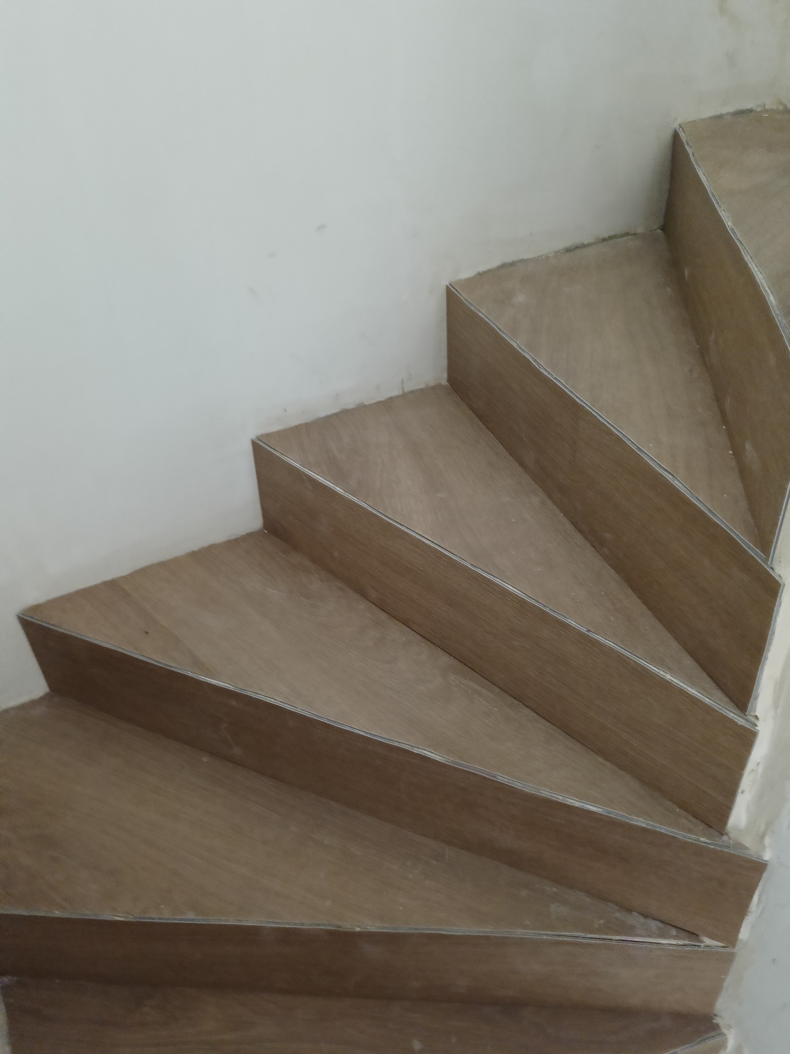 Wykończone schody z panelami o drewnianym wzorze, zabezpieczone srebrnymi listwami. Widok z góry, ukazujący detale wykończenia i strukturę materiału.