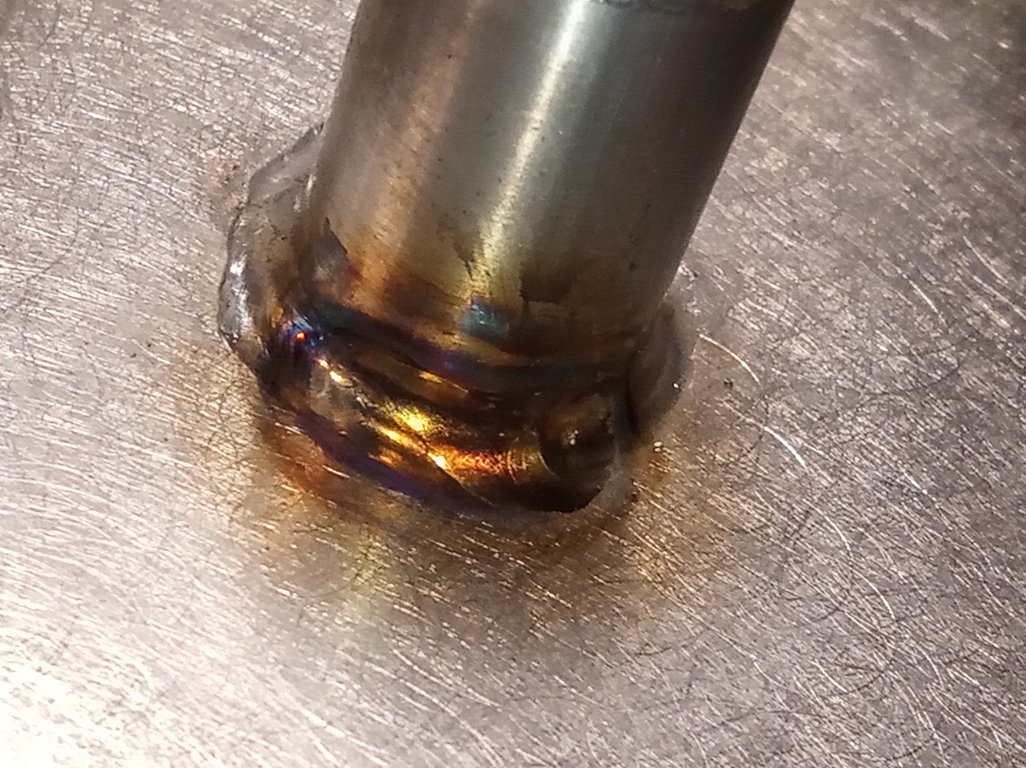 Spoina TIG z widocznymi kolorami hartowania na metalowej powierzchni. Precyzyjne łączenie rury z blachą, ukazujące umiejętności spawacza.