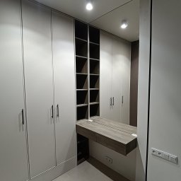 IRON GLASS SPÓŁKA Z OGRANICZONĄ ODPOWIEDZIALNOŚCIĄ - Nowoczesna garderoba z lustrem i półkami, jasne fronty szaf z minimalistycznymi uchwytami, oświetlenie punktowe, widok na wnętrze szafy z półkami.