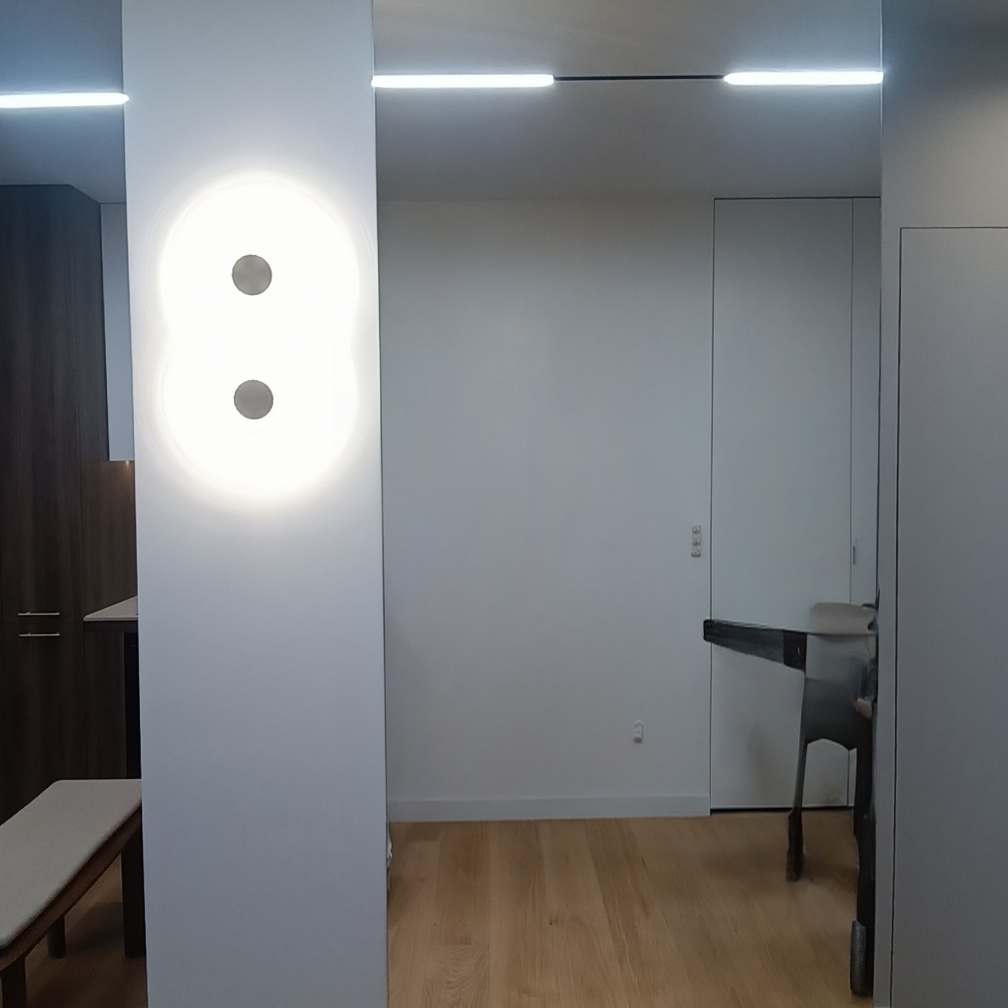 Nowoczesne wnętrze z oświetleniem LED: okrągła lampa na ścianie, minimalistyczne drzwi i drewniana podłoga. Jasne, przestronne pomieszczenie.