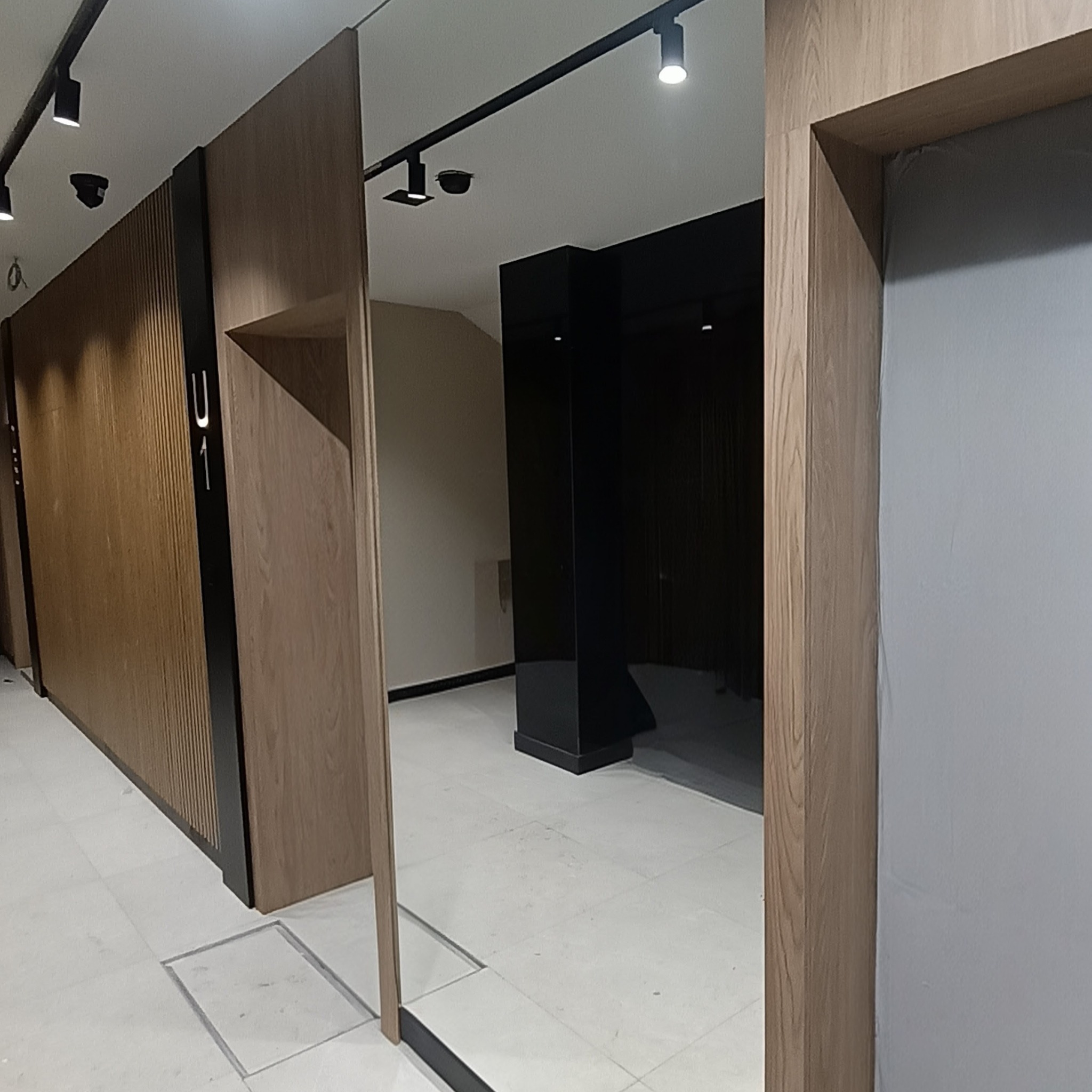 Nowoczesne drzwi z drewnianą okleiną i czarnymi akcentami, oświetlenie punktowe, minimalistyczny design wnętrza biurowego z numerem 'U1' na drzwiach.