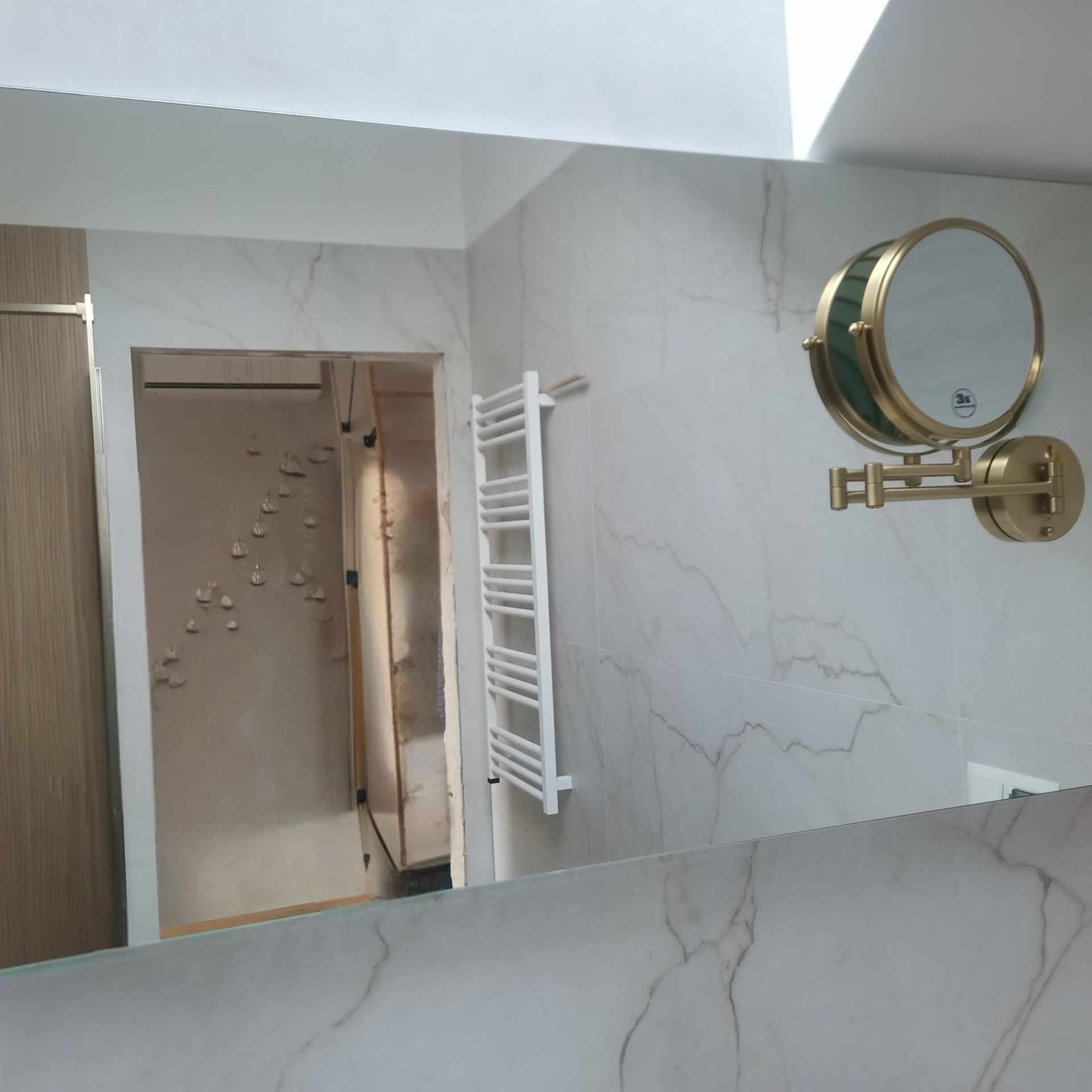 Wykończona łazienka z marmurowymi płytkami, grzejnikiem drabinkowym i lustrem powiększającym na ścianie. Widoczne odbicie remontowanego pomieszczenia w lustrze.