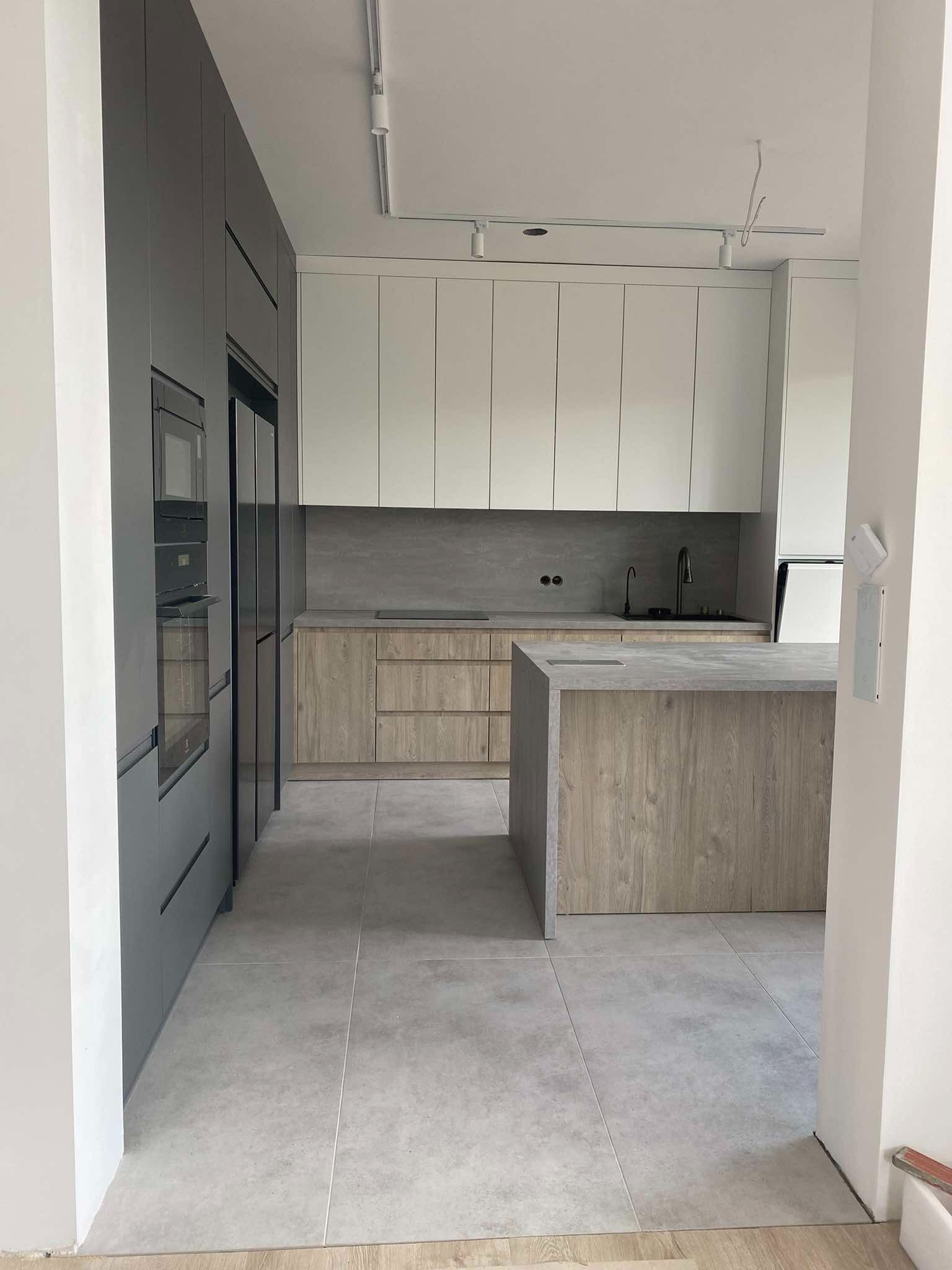 Nowoczesna kuchnia z szarymi i drewnopodobnymi frontami, wyspą kuchenną i oświetleniem szynowym.