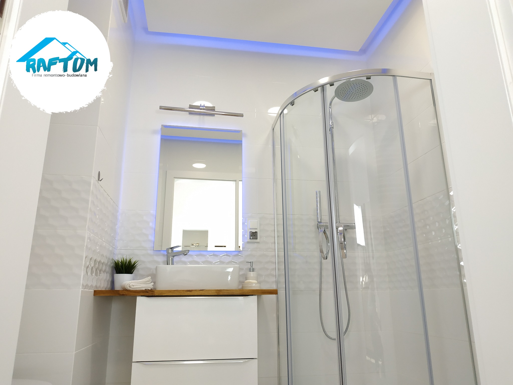 Nowoczesna, jasna łazienka po remoncie z kabiną prysznicową, umywalką nablatową na drewnianym blacie, białymi płytkami z geometrycznym wzorem i podświetleniem LED na suficie.