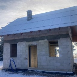 Mateusz Szynszecki - Niedokończony dom z białego bloczka, z oknami i drzwiami bez osadzenia, pokryty śniegiem, otoczony zimowym krajobrazem z drzewami i polem.