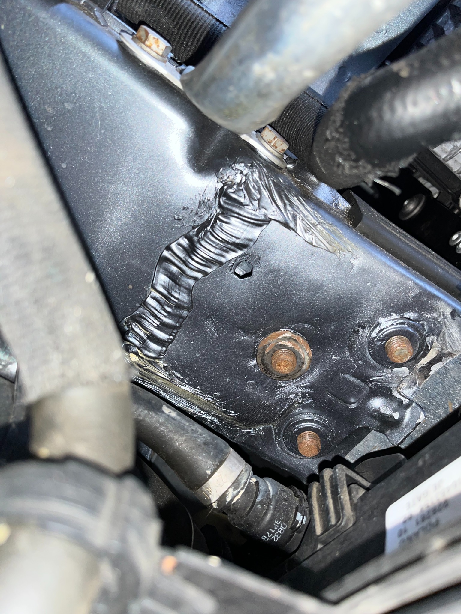 Spojenie spawane na czarnej metalowej konstrukcji w komorze silnika, widoczne ślady korozji na śrubach mocujących.