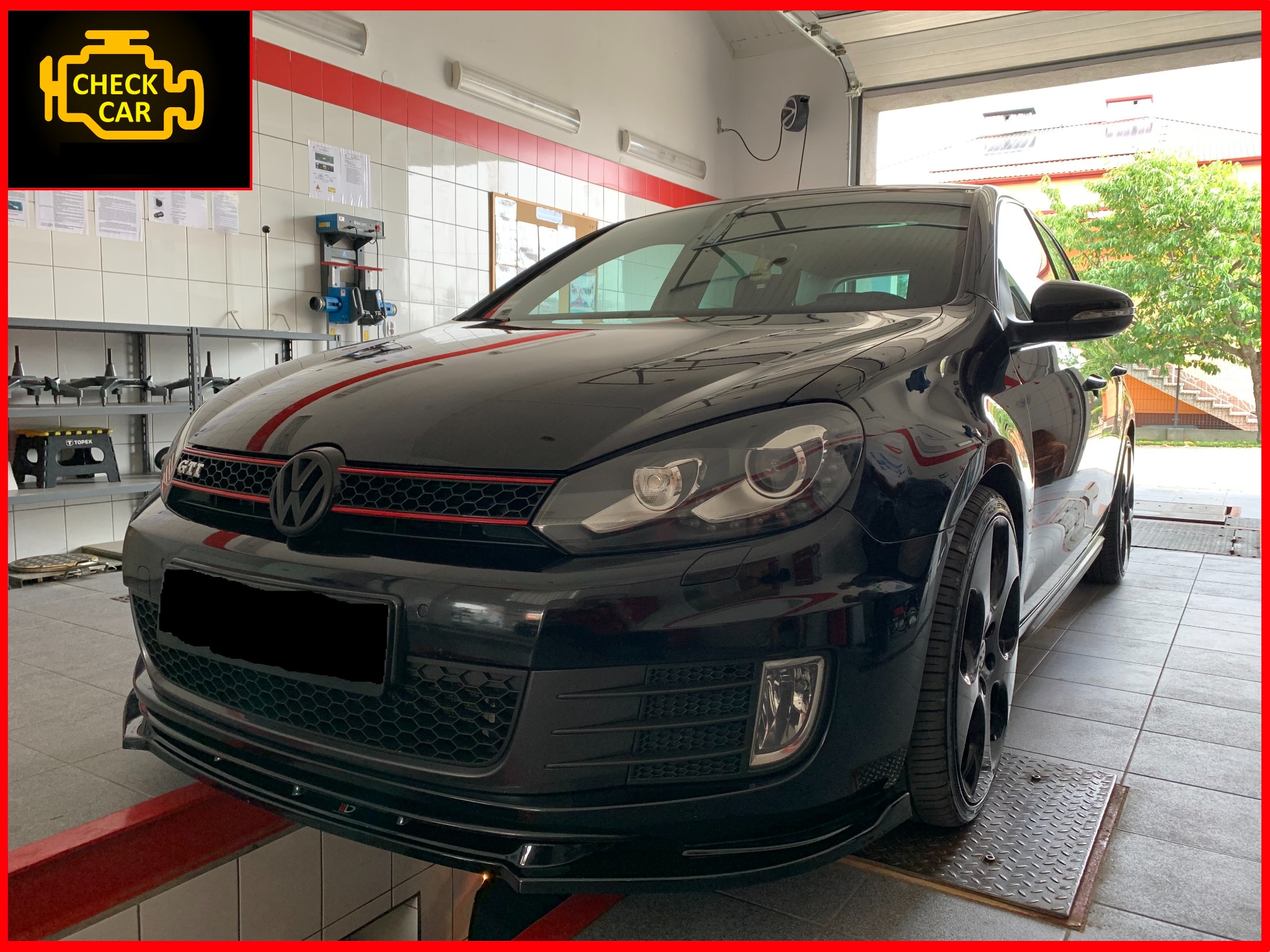 Czarny Volkswagen Golf GTI na podnośniku w warsztacie, widoczne narzędzia i wyposażenie diagnostyczne w tle.