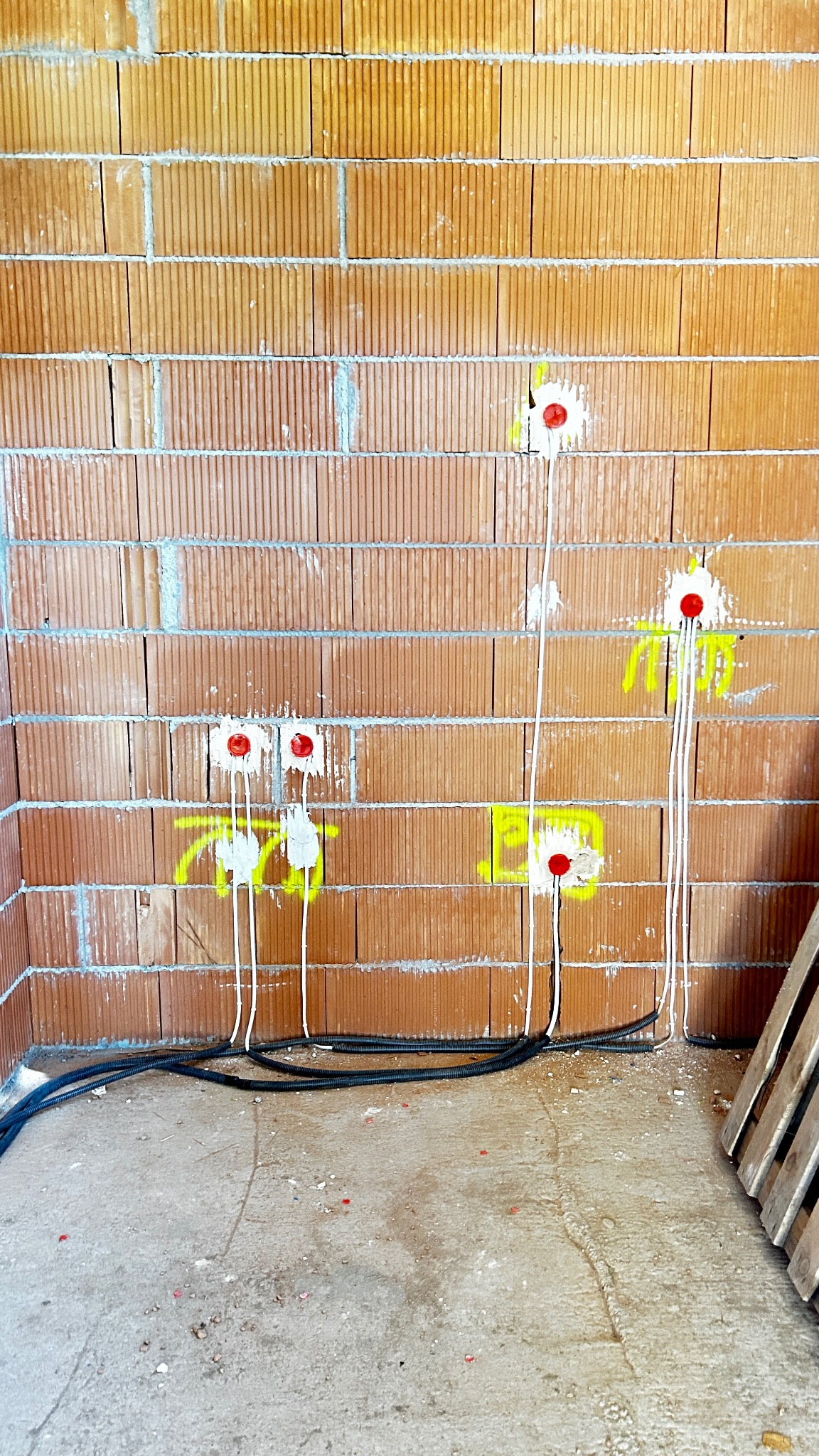Przewody elektryczne w ścianie z cegły dziurawki, przygotowane do gniazdek i włączników, oznaczone żółtą farbą. Usługi elektryczne Kraków.