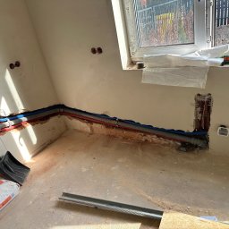 Jakub Szymanik - Wykute w ścianie rury instalacji wodnej i kanalizacyjnej w trakcie prac instalacyjnych w miejscowości Prostyń, widoczny fragment okna i materiały budowlane.