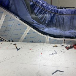 DeLift Łukasz Czechowski - Montaż schodów ruchomych: widoczne narzędzia, elementy konstrukcyjne zabezpieczone folią ochronną Novacel, częściowo ułożona podłoga z płytek.