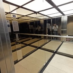 DeLift Łukasz Czechowski - Wnętrze windy z lustrzanymi ścianami, widoczny panel sterowania i odbicie osoby robiącej zdjęcie, jasne oświetlenie sufitowe.