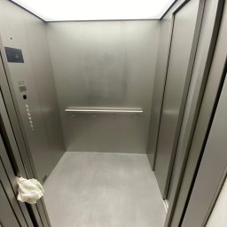 DeLift Łukasz Czechowski - Wnętrze windy z metalowymi ścianami, oświetleniem LED i panelem sterowania po lewej stronie, widok z dołu.