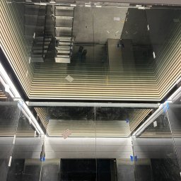 DeLift Łukasz Czechowski - Wnętrze windy w trakcie montażu, widoczne metalowe schody w szybie windy, zabezpieczone elementy i odblaski światła.