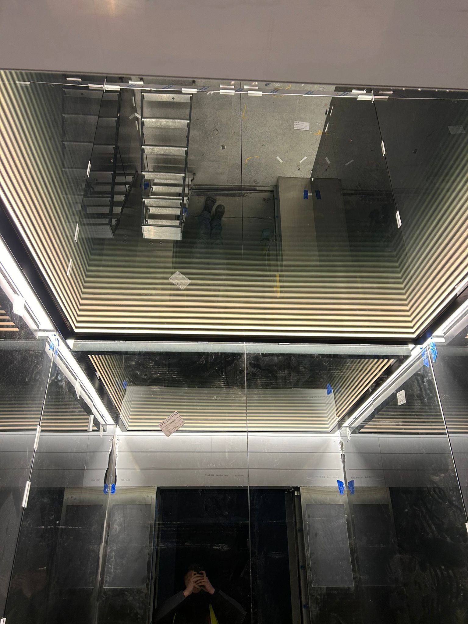 Wnętrze windy w trakcie montażu, widoczne metalowe schody w szybie windy, zabezpieczone elementy i odblaski światła.