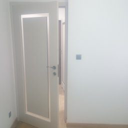Jacek Czarnecki - Otwarta, biała, nowoczesna stolarka drzwiowa z przeszkleniem w minimalistycznym wnętrzu. Widoczny fragment podłogi i ściany z włącznikiem.