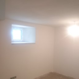 Jacek Czarnecki - Pomalowane na biało wnętrze pokoju z oknem w ścianie. Na podłodze widoczne ślady po pracach wykończeniowych. Świeżo wykończone ściany i sufit.