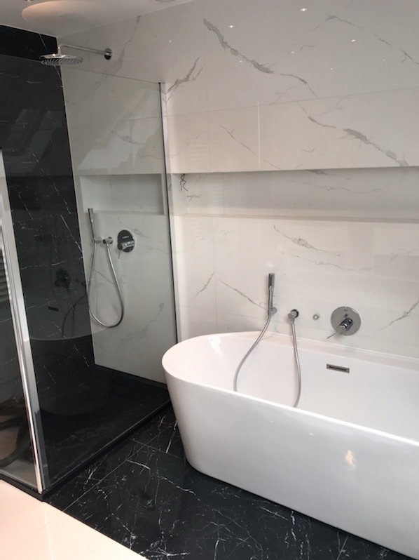 Nowoczesna łazienka z czarno-białymi marmurkowymi płytkami, kabiną prysznicową typu walk-in i wolnostojącą białą wanną.
