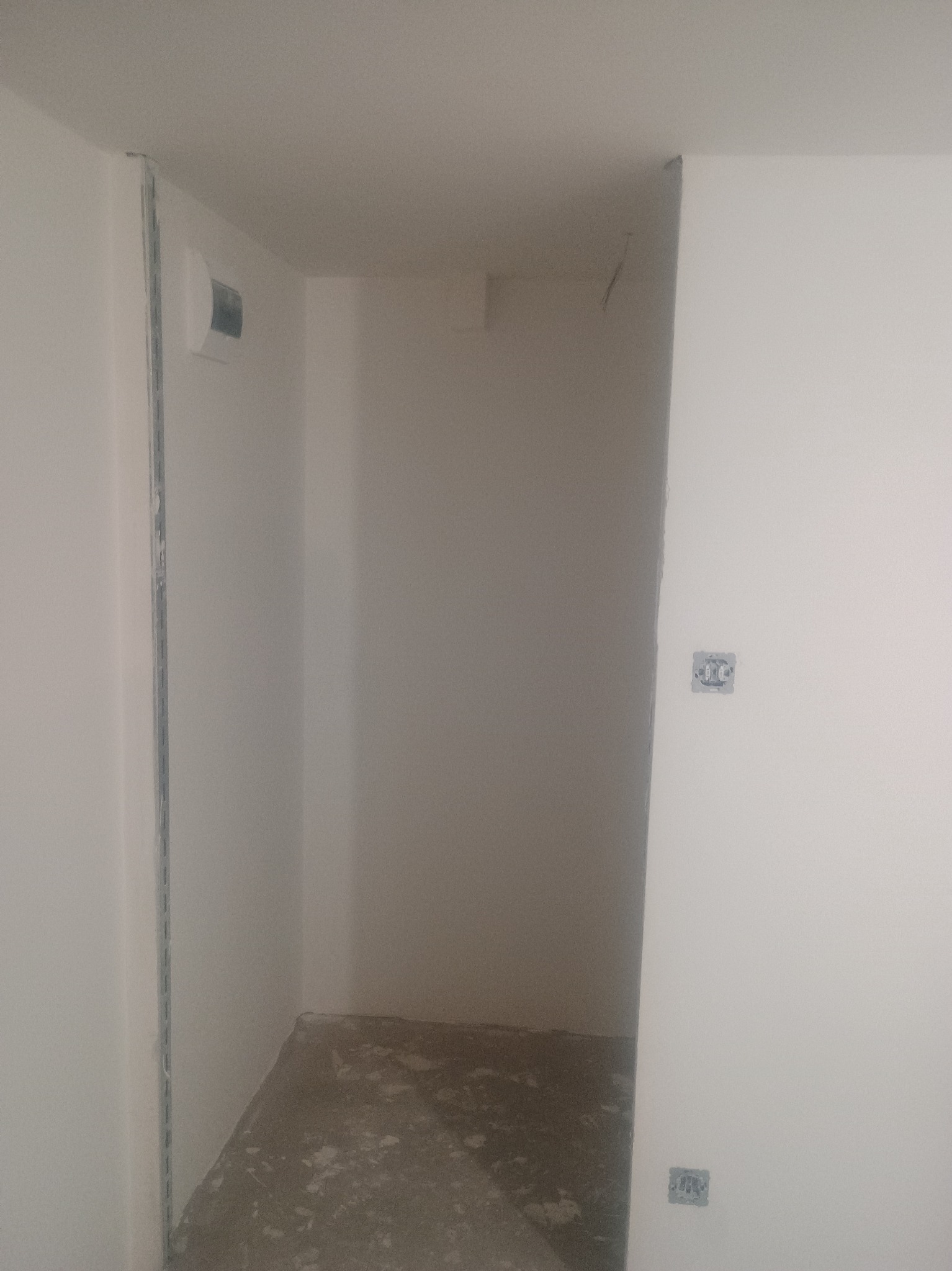 Wnętrze w trakcie prac wykończeniowych: białe ściany, surowa podłoga, widoczne puszki elektryczne i listwy montażowe. Minimalistyczny kadr z bliska.