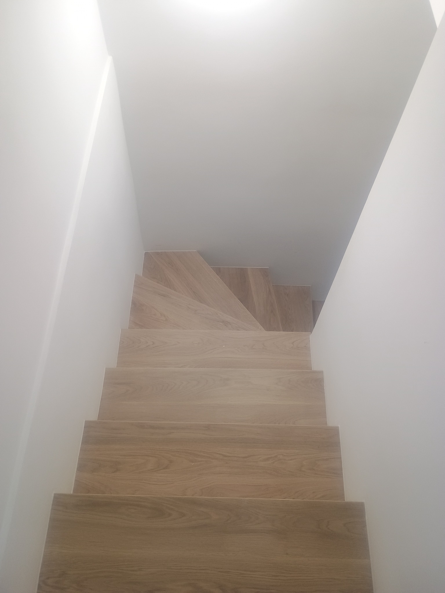 Jasne, drewniane schody w białym korytarzu, widok z góry. Minimalistyczny design, proste linie, neutralna kolorystyka. Nowoczesne wykończenie wnętrz.