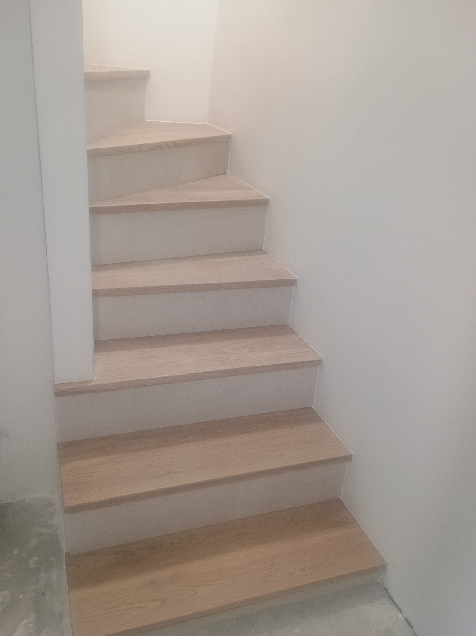 Jasne, drewniane schody w minimalistycznym wnętrzu. Widoczne detale wykończenia i subtelne oświetlenie podkreślają nowoczesny charakter.