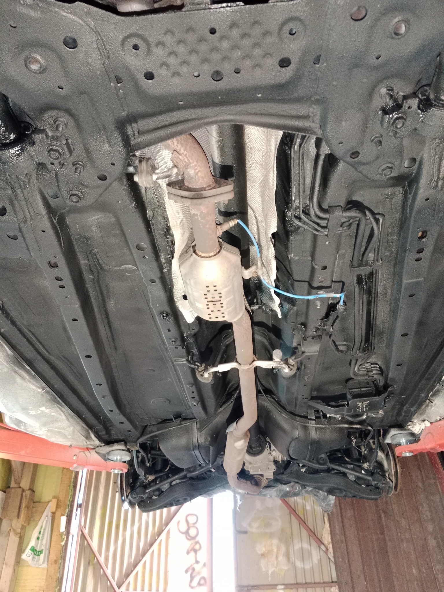 Spód samochodu na podnośniku po zabezpieczeniu antykorozyjnym, widoczny układ wydechowy i elementy zawieszenia pokryte czarną powłoką ochronną.