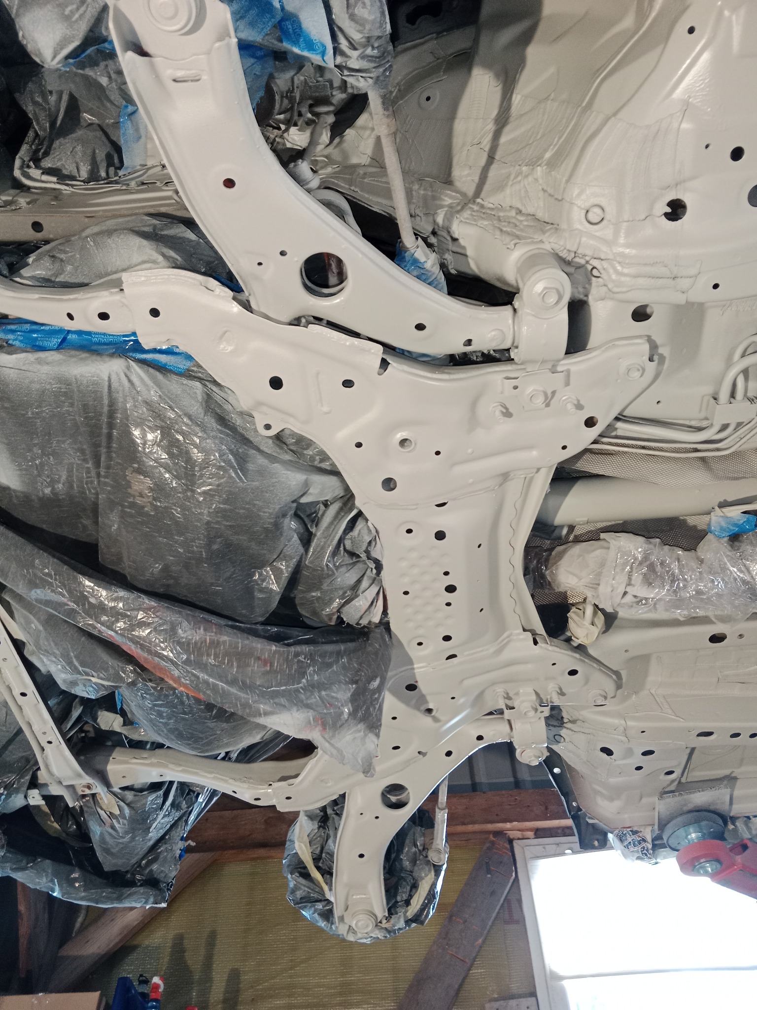 Podwozie samochodu po zabezpieczeniu antykorozyjnym i pomalowaniu na biało; widoczne elementy zawieszenia zakryte folią ochronną.