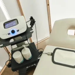 Aparat do fizykoterapii Tecaris z elektrodą na leżance, obok butelki z żelem kontaktowym i akcesoriami, w gabinecie zabiegowym.