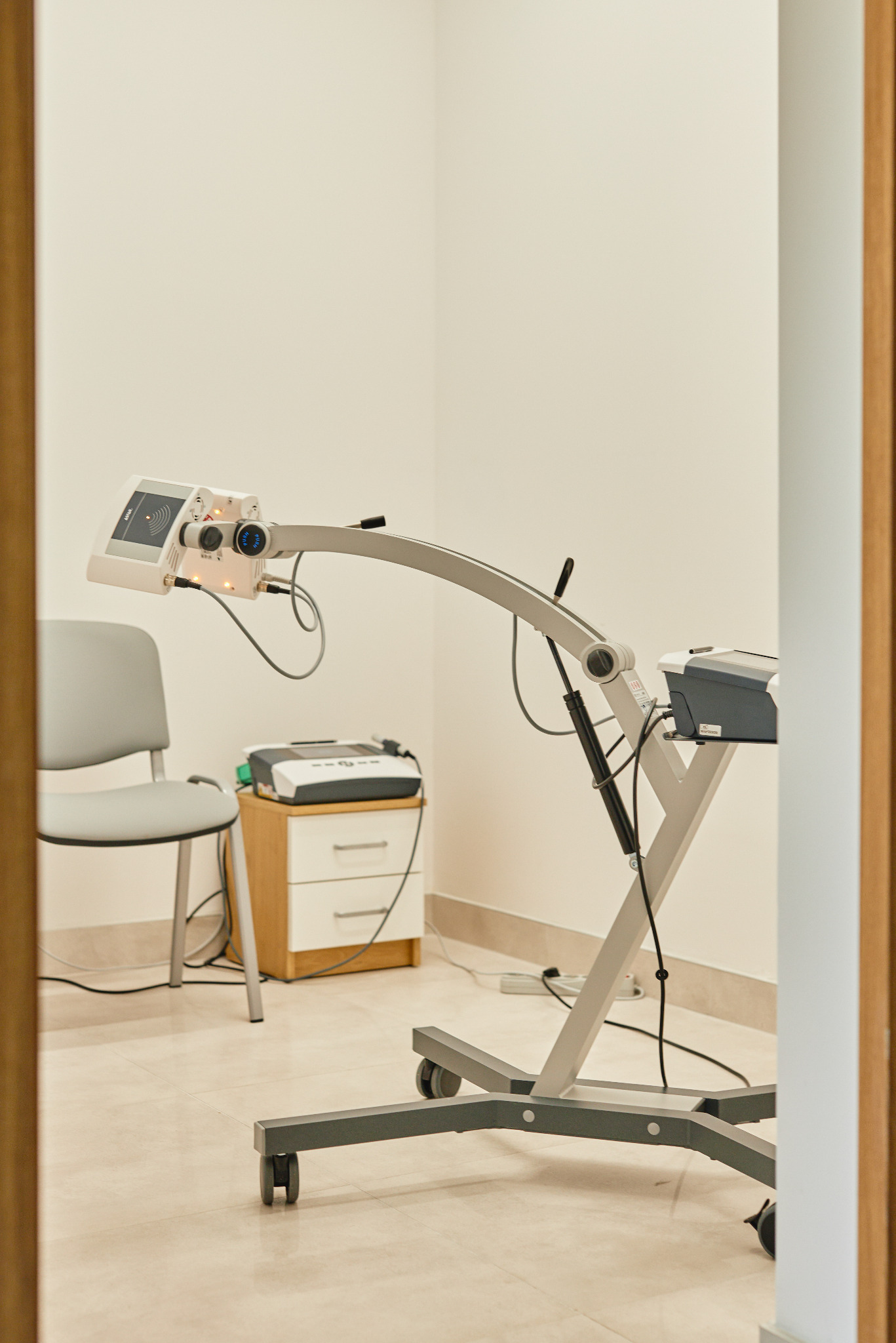 Sprzęt do terapii światłem ustawiony w gabinecie, widoczny fotel i szafka z urządzeniami w tle.