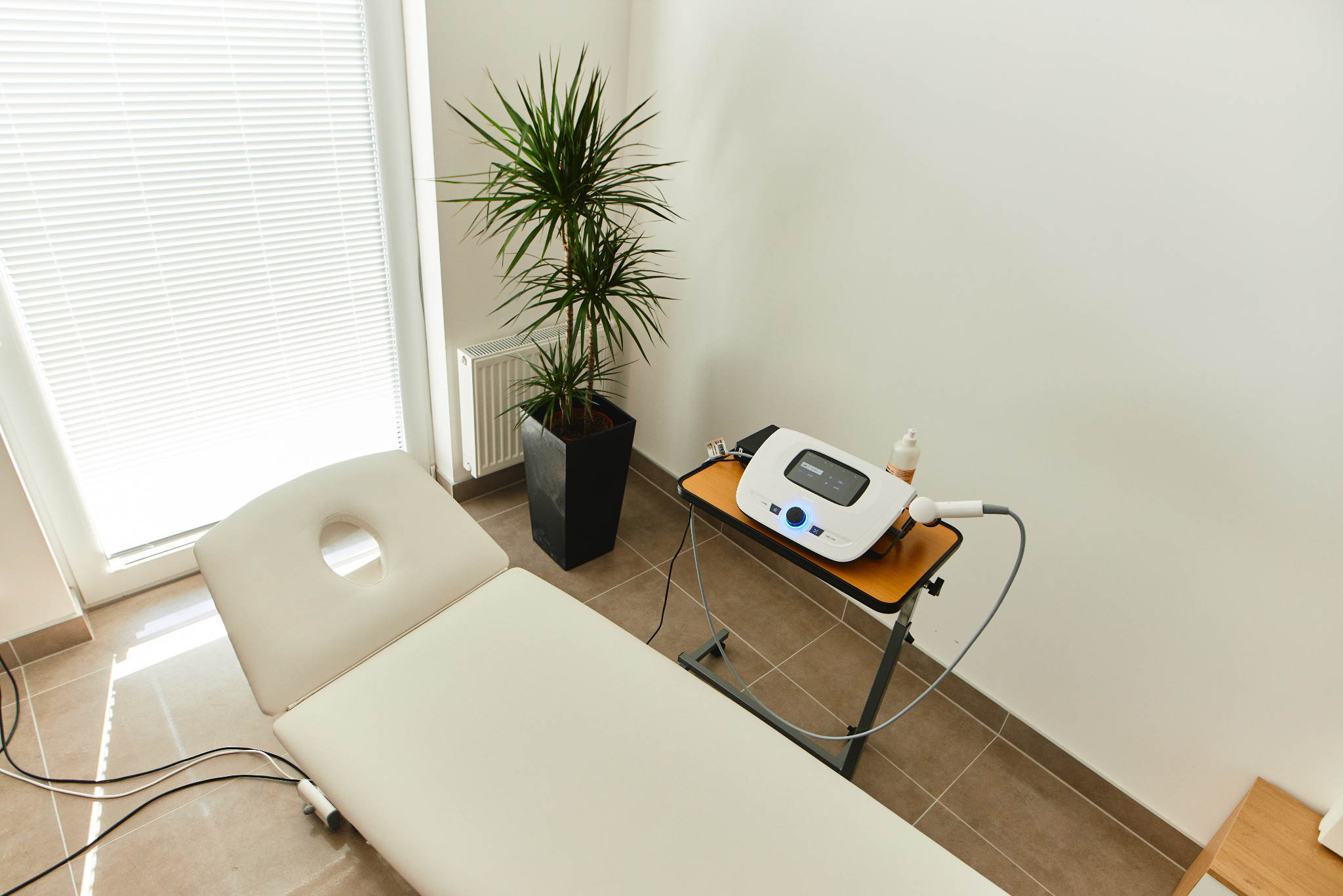Jasny gabinet z kozetką do terapii, aparaturą do zabiegów i rośliną doniczkową, widok z góry.