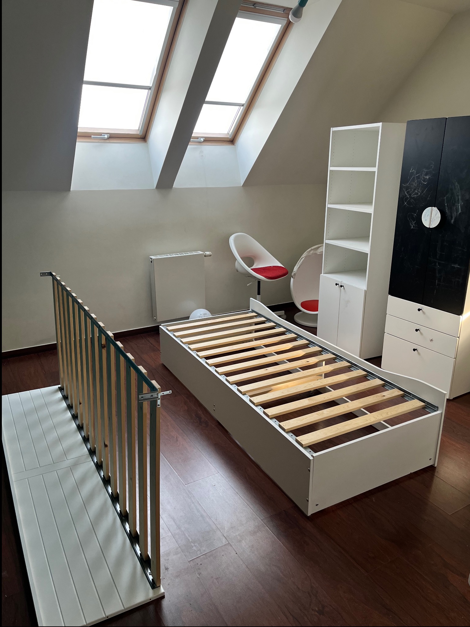 Rozłożone łóżko z drewnianym stelażem w pokoju na poddaszu, obok szafki i krzesła, przygotowane do transportu.