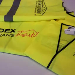 Żółte kamizelki odblaskowe z nadrukowanym logo firmowym Bedex Trans z symbolem czerwonego byka oraz B3 Entreprenad z motywem budowlanym na jasnym tle.