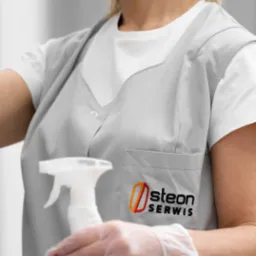 Pracownica w szarym uniformie z logo firmy 'Osteon Serwis' trzyma biały spryskiwacz, dłoń w przezroczystej rękawiczce, przygotowana do pracy.