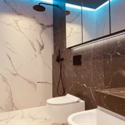 Elegancka łazienka z marmurowymi płytkami, podwieszaną toaletą i bidetem. Czarna deszczownica i oświetlenie LED dodają nowoczesnego charakteru.