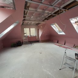 Pavlo Tovstyha - Poddasze w trakcie adaptacji: różowe płyty na skosach, metalowa konstrukcja sufitu, okna dachowe z folią. Widoczne drabiny i narzędzia.