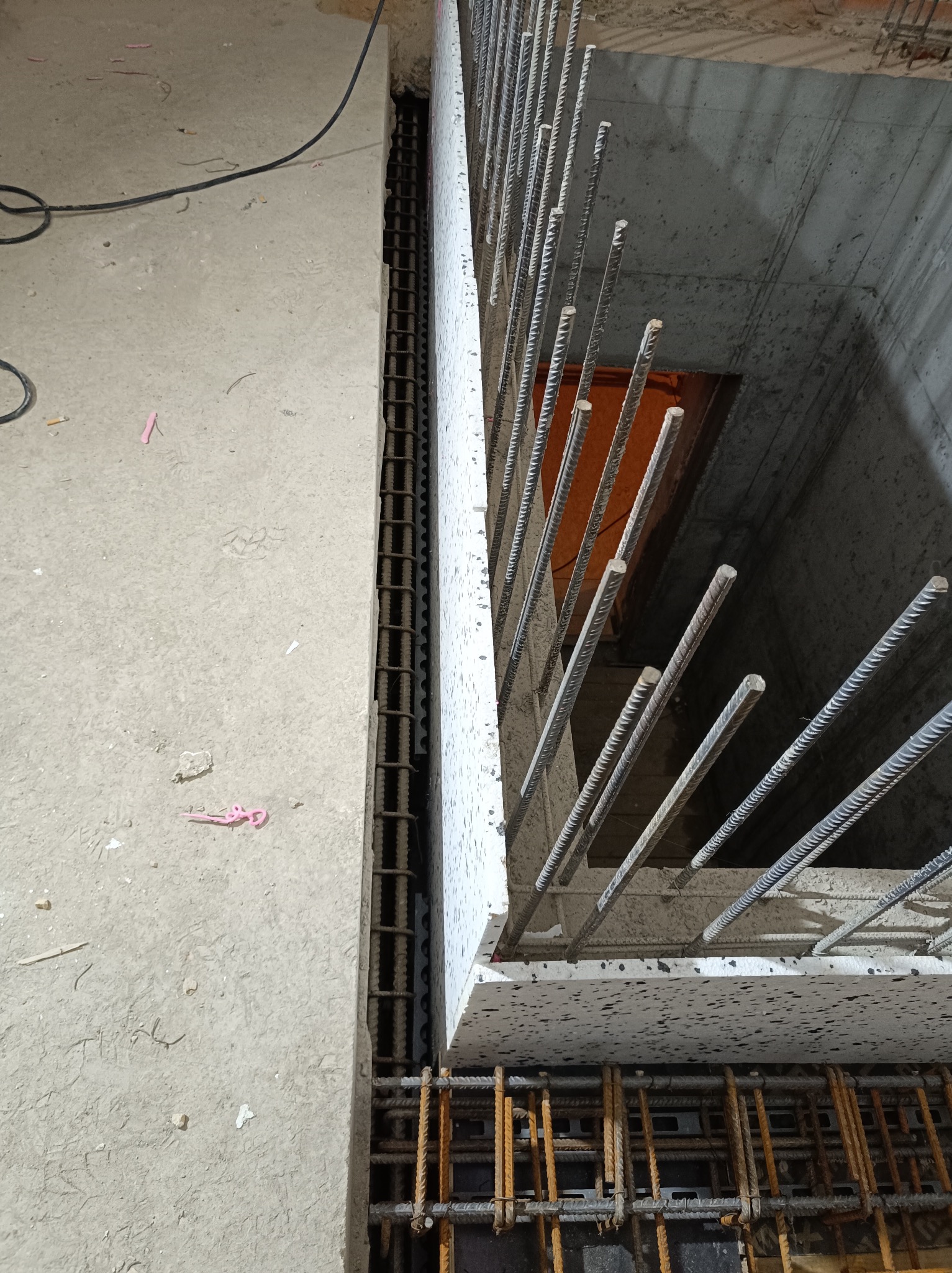 Zbrojenie pionowe i poziome w szalunku, widoczne pręty żebrowane i betonowe ściany fundamentowe w trakcie budowy.