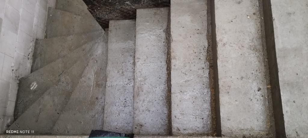 Surowe betonowe schody w trakcie budowy z widocznymi niedoskonałościami i śladami po szalunku, ujęcie z góry.