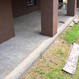 Remonty I wykonczenia wnetrz - Wykończony podcień domu z brązową elewacją typu baranek, betonową podłogą i widocznymi elementami ogrodu.