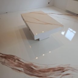 Remonty I wykonczenia wnetrz - Błyszcząca podłoga z żywicy epoksydowej w odcieniach bieli i brązu, imitująca marmur, z widoczną nogą stołu i fragmentem buta w rogu.