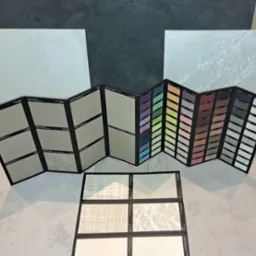 Ekspozycja próbek kolorów i faktur gładzi dekoracyjnych na tle paneli z różnymi wykończeniami.