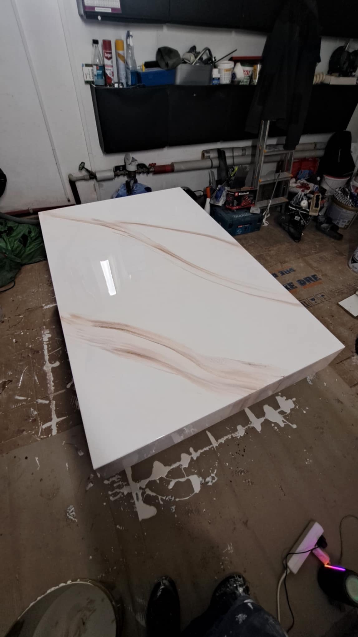 Biały blat z marmurkowym wzorem w odcieniach beżu, leżący w pomieszczeniu w trakcie prac wykończeniowych, widoczne plamy farby na podłodze, narzędzia i akcesoria w tle.