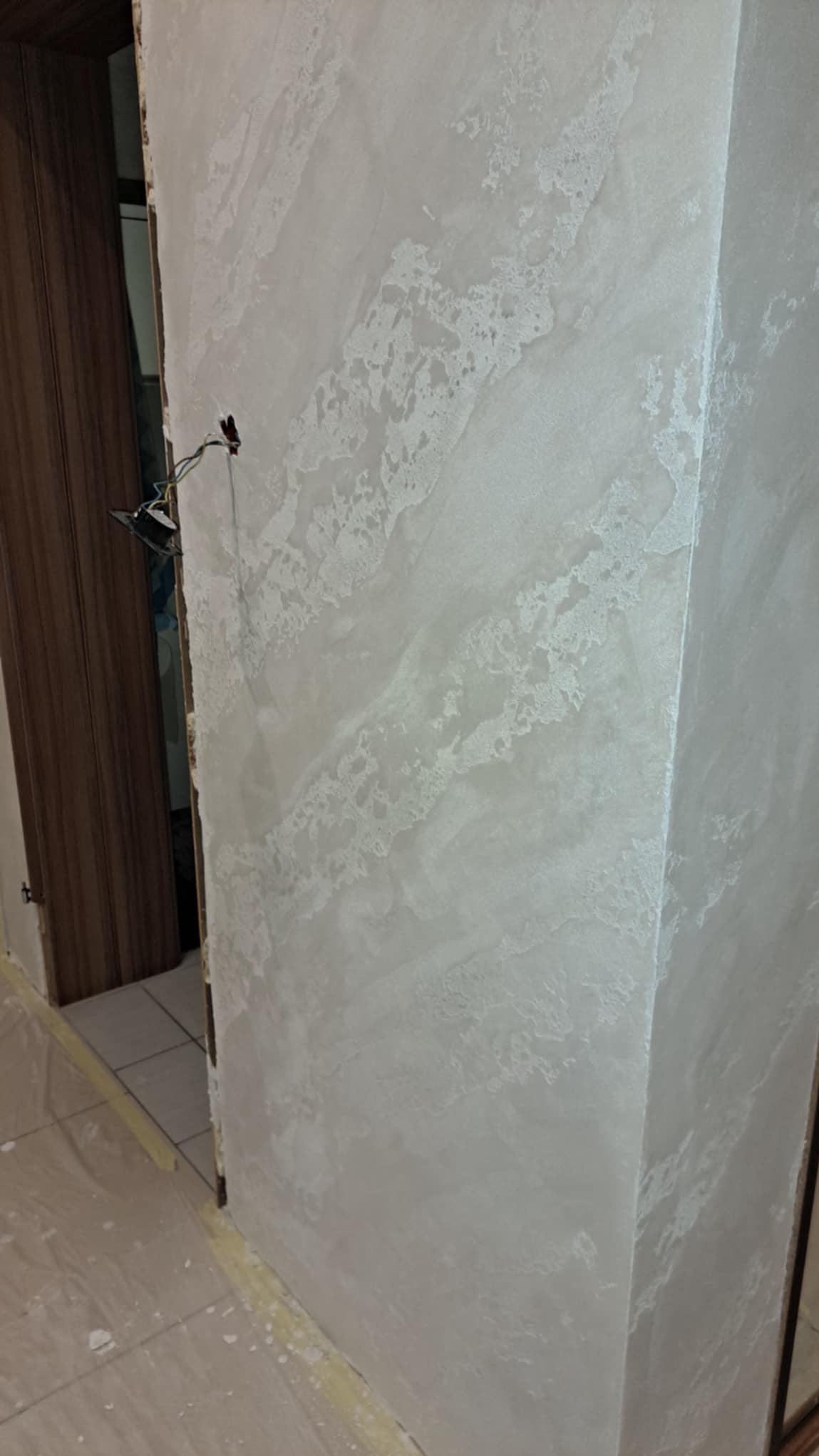 Ściana po wykonaniu gładzi dekoracyjnej z efektem marmuru, widoczne niedokończone prace elektryczne przy framudze drzwi.