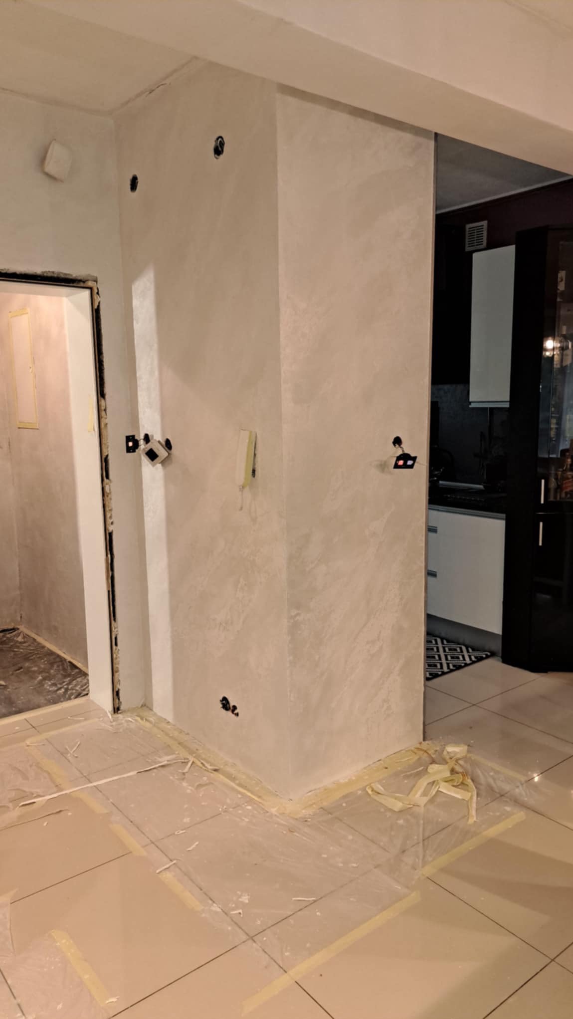 Ściana po nałożeniu gładzi dekoracyjnej z widocznymi otworami na gniazdka elektryczne i zabezpieczoną folią podłogą.