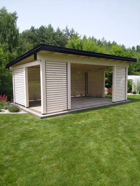 Nowoczesna, otwarta altana z drewnianymi żaluzjami bocznymi, otoczona zadbanym trawnikiem i zielenią.