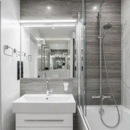 Nowoczesna łazienka z umywalką na szafce z szufladami, kabiną prysznicową z parawanem nawannowym, szarą płytką imitującą kamień i lustrem z oświetleniem LED.