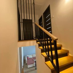 Uslugi spawalniczo monterskie - Nowoczesne schody drewniane z czarną, metalową balustradą w minimalistycznym wnętrzu. Widok z góry, oświetlenie punktowe podkreśla strukturę drewna.