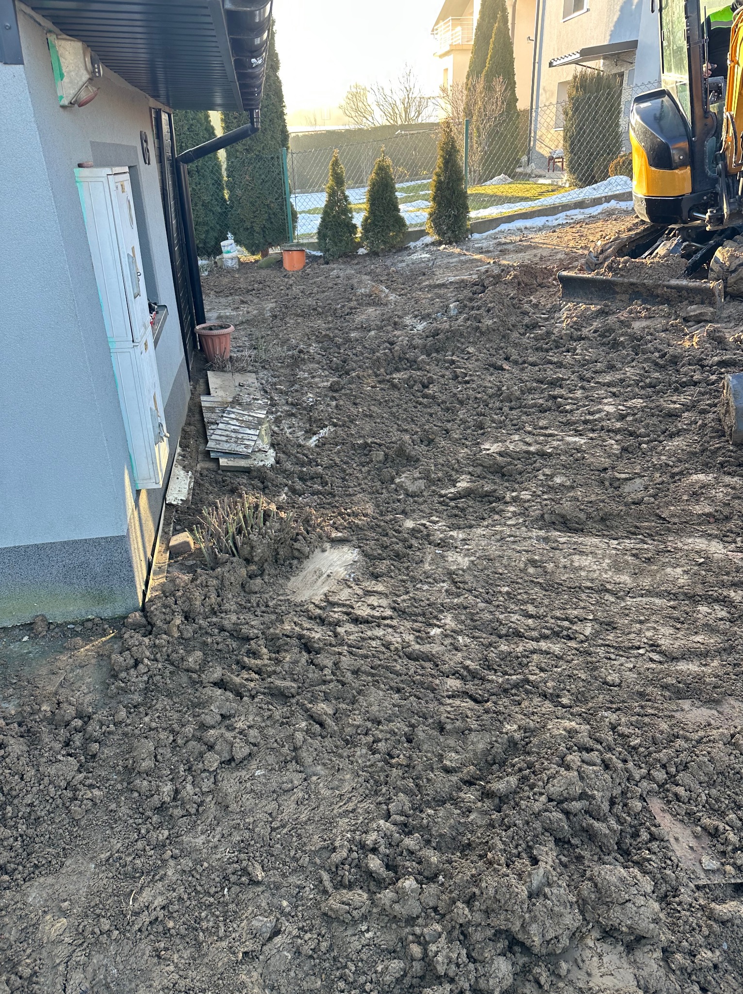 Wykop pod przyłącze wod-kan w ogrodzie, widoczny mini-koparka i przygotowany teren pod instalację. Świecące słońce w tle.