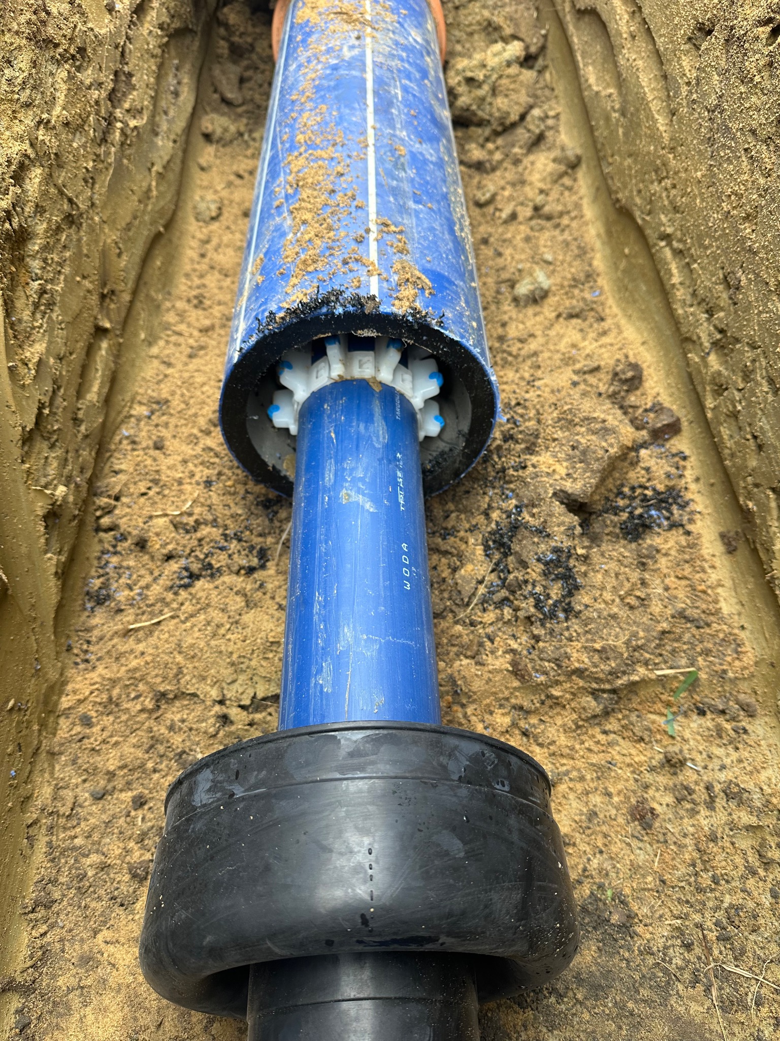 Niebieskie rury wodociągowe w wykopie z piaskiem, widoczne elementy złączek i uszczelnień. Ujęcie z góry, podkreślające detale instalacji.