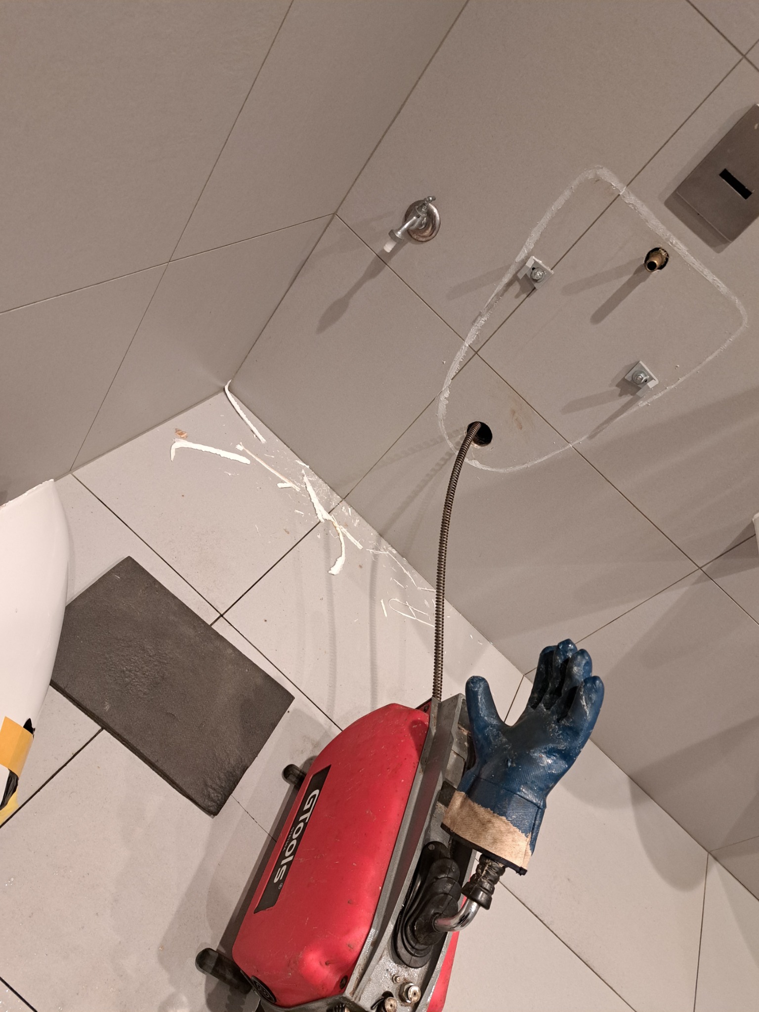 Udrażnianie zatkanej rury w łazience z użyciem specjalistycznego sprzętu GTools. Widoczne pozostałości po zatorze i otwór w podłodze.